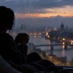 Silhouette pensive près d’une fenêtre au crépuscule, une tasse entre les mains